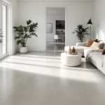 Moderne woonkamer met een matte, grijze betonlook PVC-vloer, Scandinavische meubels en veel natuurlijk licht.